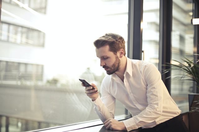 Photo of Man in White Dress Shirt Holding Phone Near Window